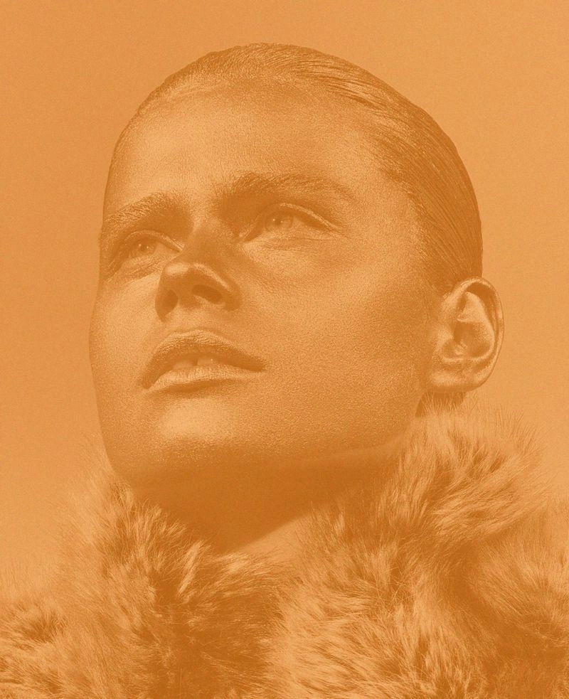 Close-up portrait of a model with slicked-back hair and a furry collar, rendered in a warm monochromatic orange tone.