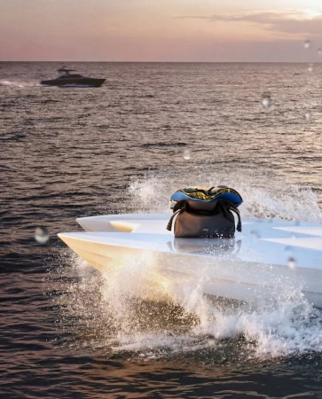 A white speed boat cuts through ocean water with a bag on board, another boat is in the background beneath a pastel sunset sky.