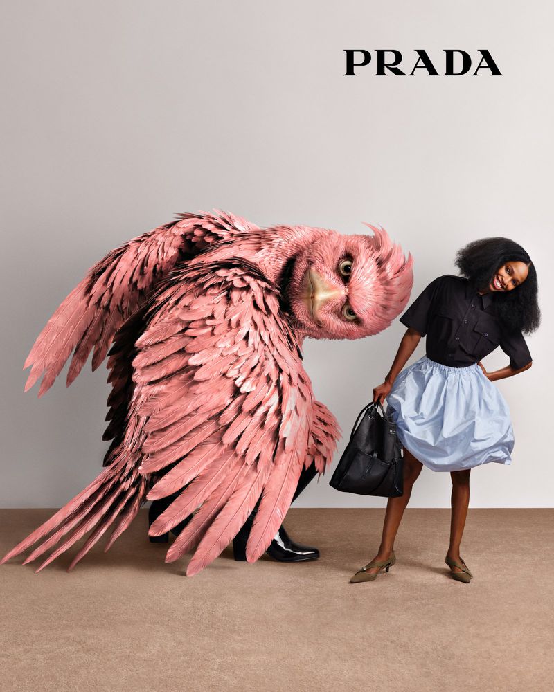 Fashion editorial shot showcasing a woman in a light blue skirt and a large, anthropomorphic pink bird-like creature for PRADA campaign.