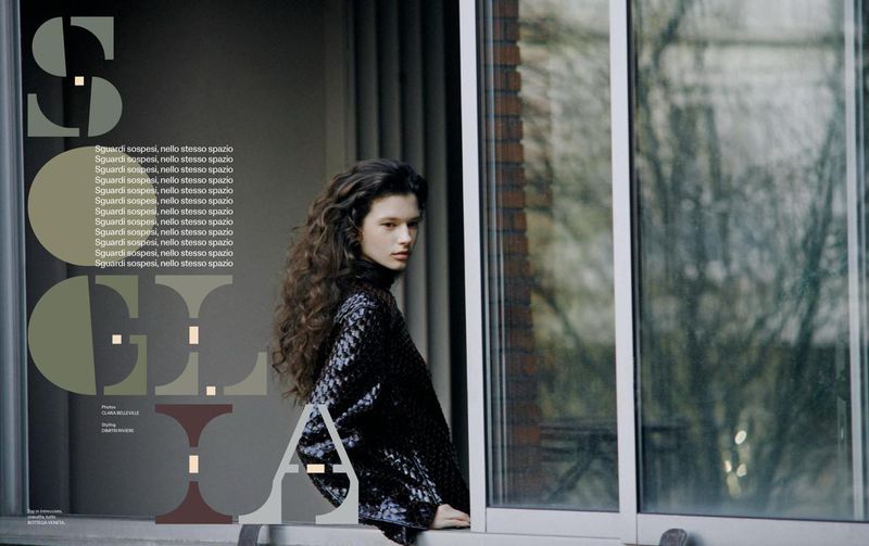 Portrait of woman with curly hair in black turtleneck standing in front of window with reflected trees and editorial text overlay.