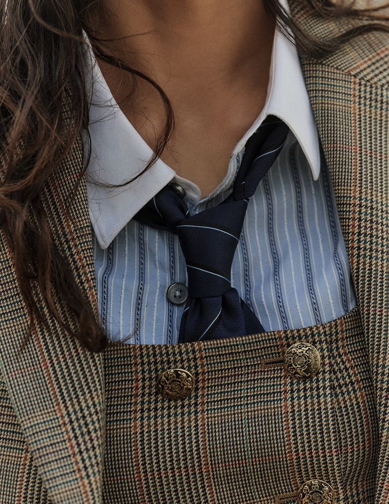 Close-up of a model wearing a plaid blazer, white-collared shirt, blue striped button-down shirt, and a navy tie.