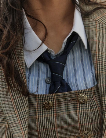 Close-up of a model wearing a plaid blazer, white-collared shirt, blue striped button-down shirt, and a navy tie.