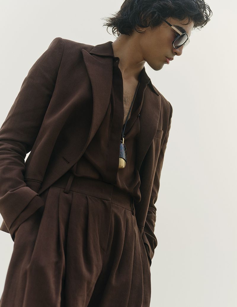 Model in brown suit and dark sunglasses against a seamless white background for Vogue Scandinavia