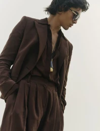 Model in brown suit and dark sunglasses against a seamless white background for Vogue Scandinavia
