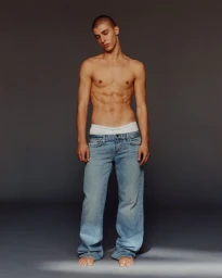 Shirtless man with short hair wearing light wash blue denim jeans against a dark grey seamless studio backdrop