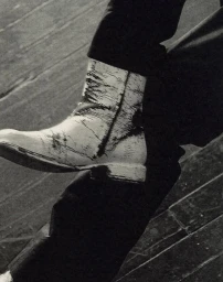 Close-up of a textured white boot and dark trousers on a wooden floor, shot for 321 Magazine.