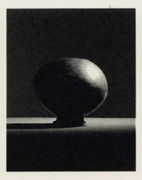 Close-up of a rounded dark ceramic vessel resting on a surface under dramatic low-key lighting for 321 Magazine.