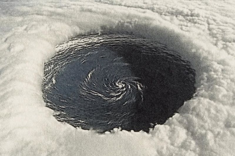 Overhead view of a hurricane eye with swirling dark ocean water surrounded by thick, bright white clouds forming the storm's structure.
