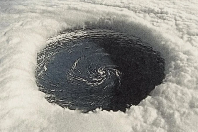 Overhead view of a hurricane eye with swirling dark ocean water surrounded by thick, bright white clouds forming the storm's structure.
