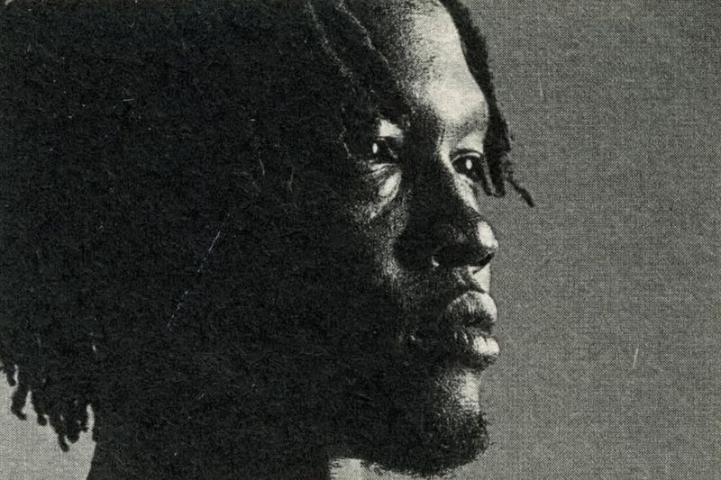 Close-up side profile portrait of a Black man with dreadlocks, captured in a high-contrast black and white film grain aesthetic.