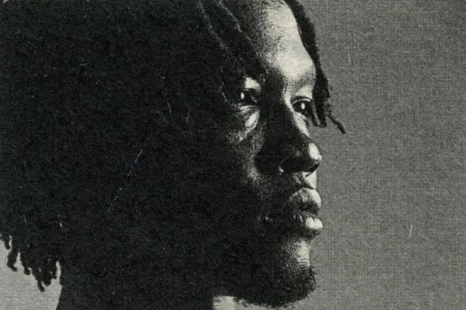 Close-up side profile portrait of a Black man with dreadlocks, captured in a high-contrast black and white film grain aesthetic.