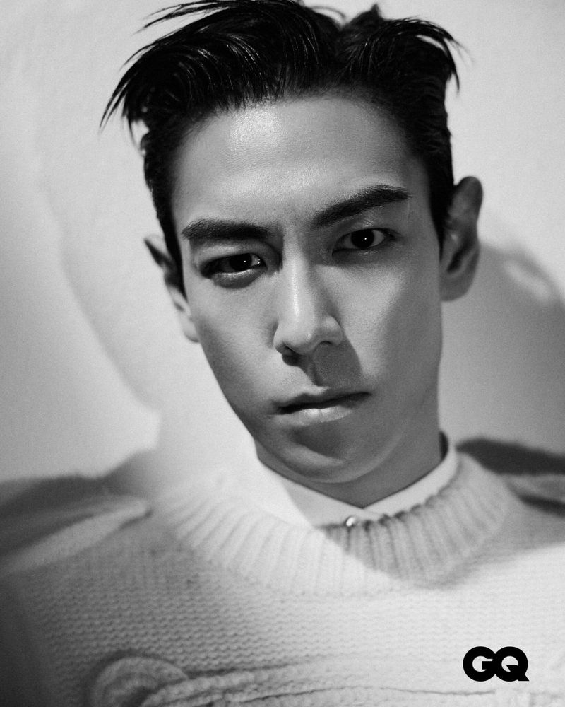 Black-and-white portrait of a man with dark hair wearing a knitted sweater, gazing intently at the camera in a photo studio setting.