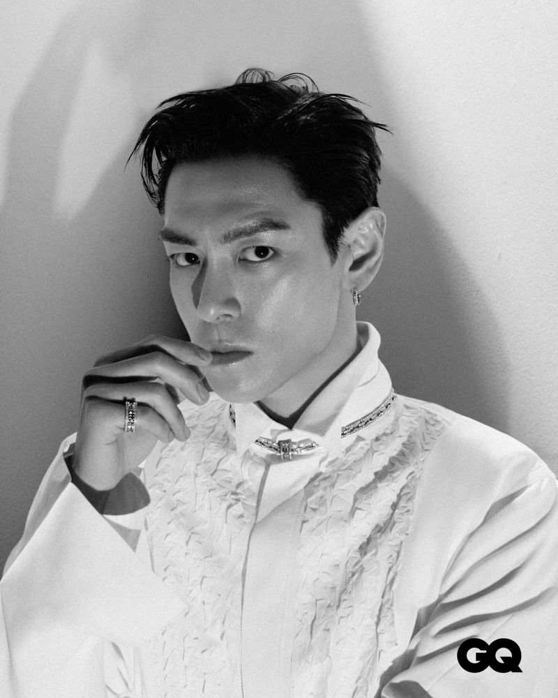 Black and white portrait of an adult male in a white dress shirt with a ruffled front, striking a pose against a neutral background.