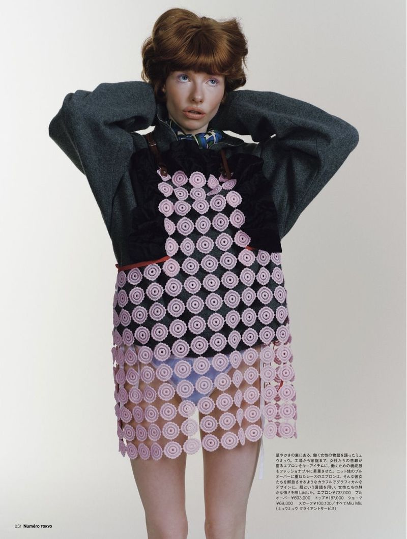 Fashion-forward redhead woman with patterned dress posing in studio, hands behind head, cool grey sweater, looking up, modern editorial.