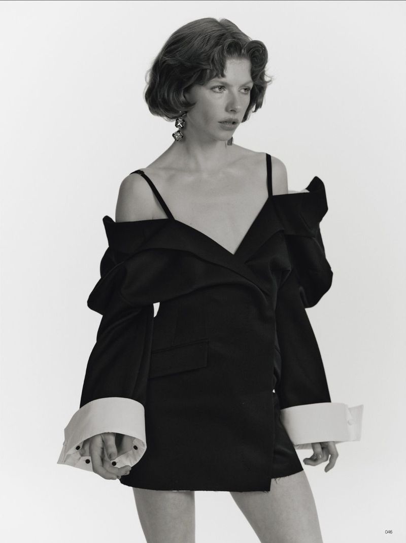 Black and white portrait of a young woman in an oversized black blazer dress with white cuffs against a white backdrop.