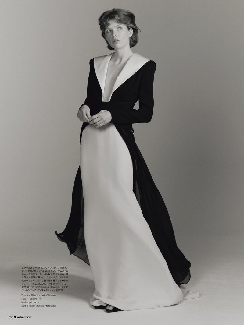 Elegant editorial shot of a model in a black and white dress with a plunging neckline, standing in a light grey studio.