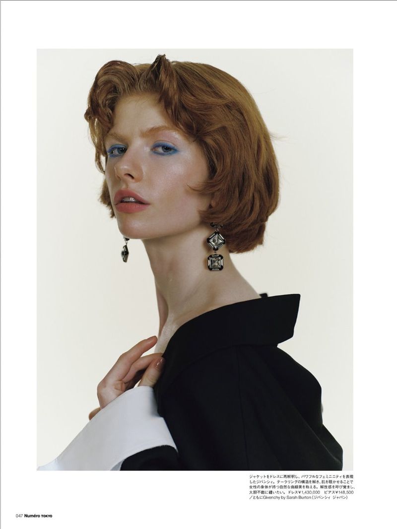 Close-up fashion shot of a young fair-skinned woman with red hair wearing a black top with a white collar and statement earrings.