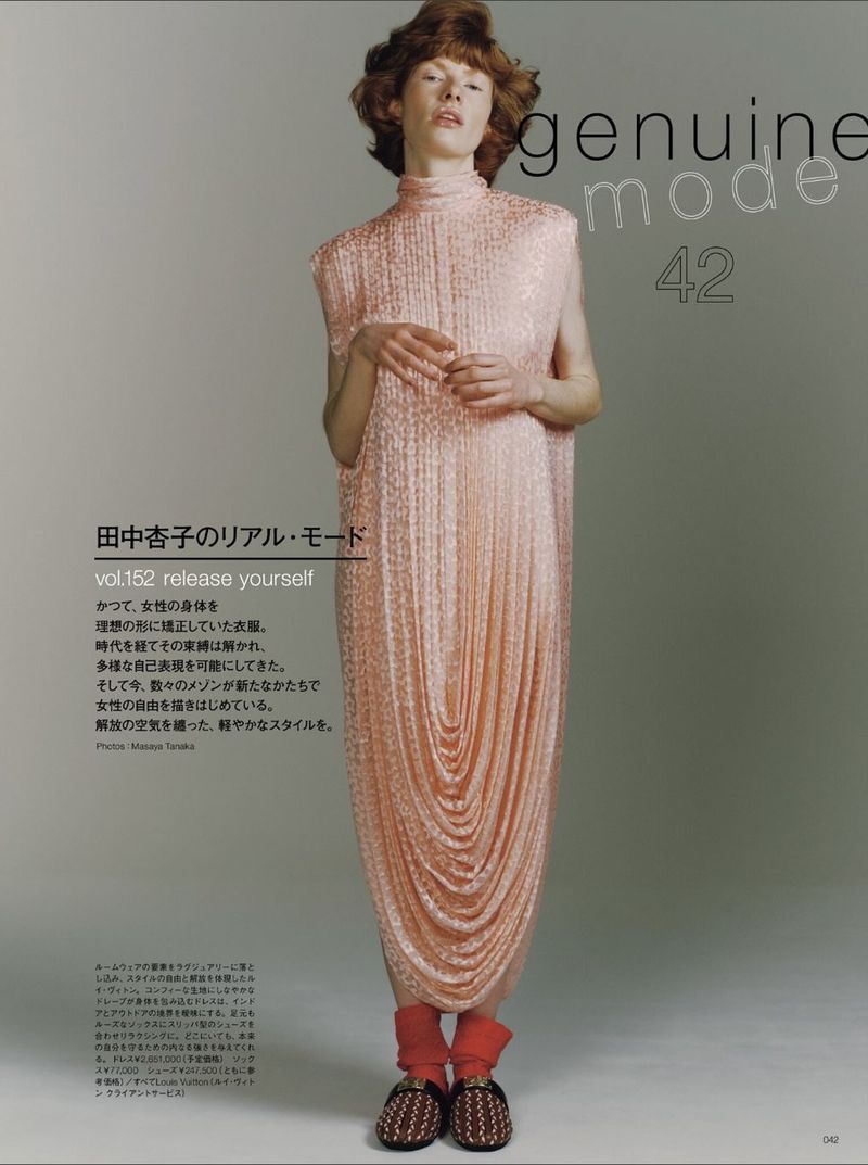 Fashion editorial shot: a slender adult woman stands in a sparkling pale pink high-neck gown with draped detailing, red socks, and moccasins.