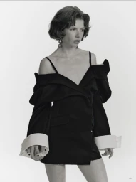 Model Edwina Preston wearing an off-the-shoulder black dress with white cuffs against a seamless white studio background.