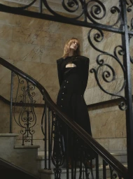 Model wearing a structured black dress on a grand marble staircase with ornate iron railings