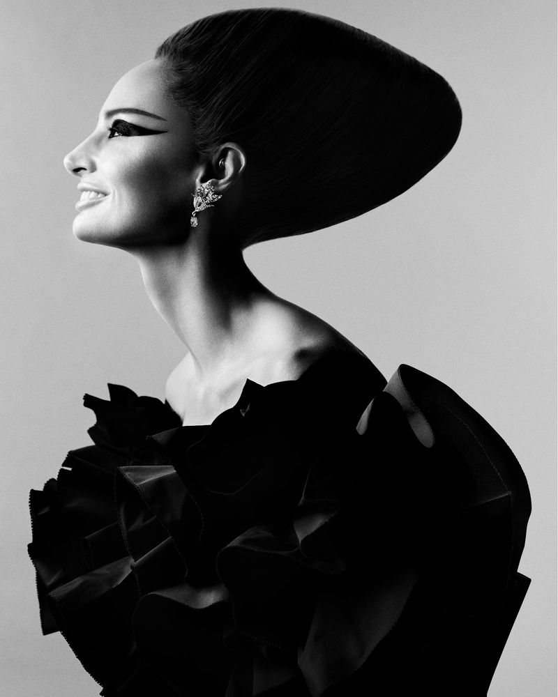 Elegant black and white portrait of a smiling woman with a voluminous hairstyle, wearing a ruffled dress and statement earrings.
