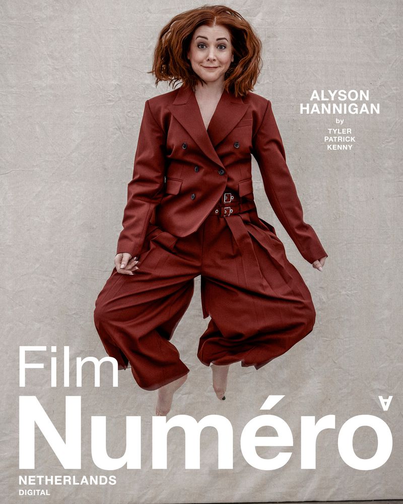 Alyson Hannigan in a burgundy suit jumping in the air on a grey background for the cover of Film Numero Netherlands Digital.
