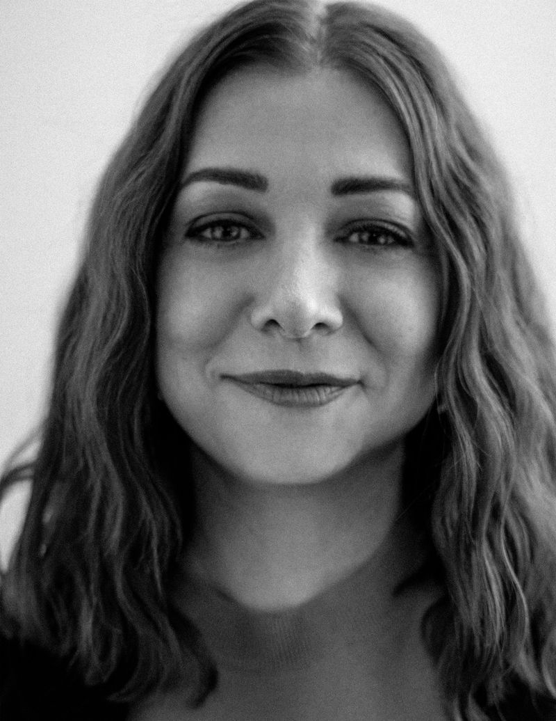 Black and white portrait of a smiling adult woman with wavy hair, facing forward in an indoor setting with neutral lighting.