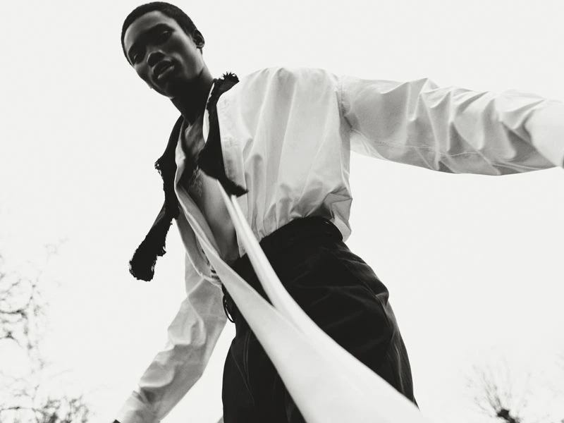 Low-angle shot of an African male model in a white shirt and dark pants against a bright sky. Fashion editorial with dramatic lighting.