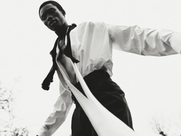 Low-angle shot of an African male model in a white shirt and dark pants against a bright sky. Fashion editorial with dramatic lighting.