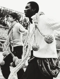 Monochrome fashion editorial image of two male models running outdoors wearing knit scarves with pom-poms for HERO Magazine.