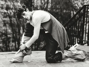 Model kneeling outdoors wearing a cap, long-sleeved top, trousers, and boots with clear heels