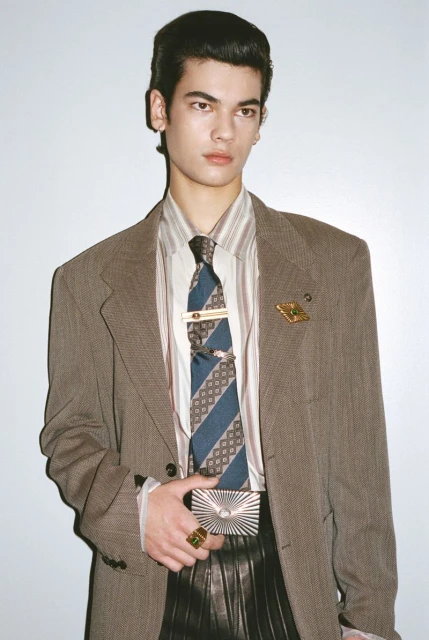 Portrait of a stylish male fashion model wearing a blazer, collared shirt, and tie while holding a metallic card holder in a studio.