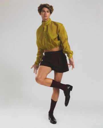 Model Luke Pearson wearing a yellow cropped jacket and dark shorts against a seamless white studio background for HERO Magazine.
