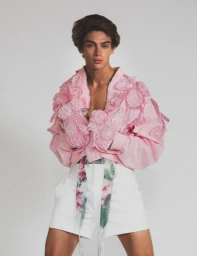 Model wearing a pink textured jacket and white shorts against a pale studio background for HERO Magazine.