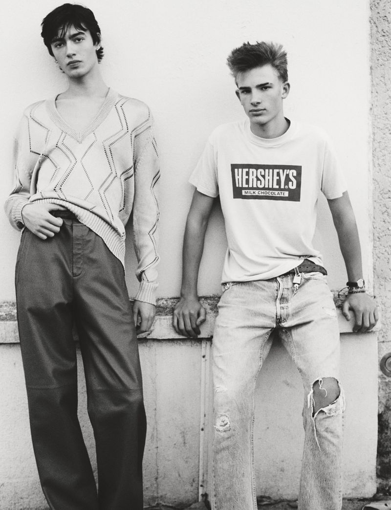 Two young men in casual fashion pose in a black and white photograph, one in a patterned sweater, one in a Hershey's t-shirt.
