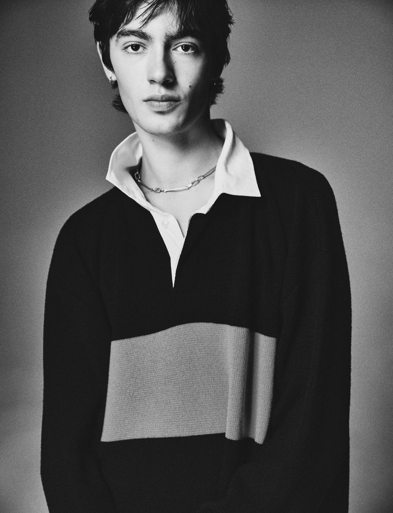 Black and white portrait of a young adult male wearing a rugby shirt and silver chain against a neutral background.