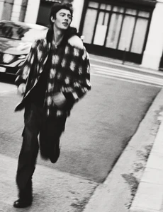 Young man in a patterned jacket running along a city street in a black and white fashion editorial photograph.