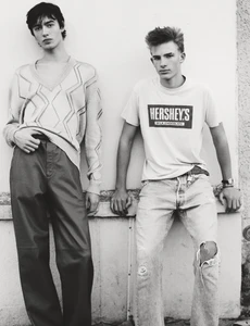 Two young male models posing against a light wall for HERO Magazine, wearing casual streetwear and patterned knitwear.