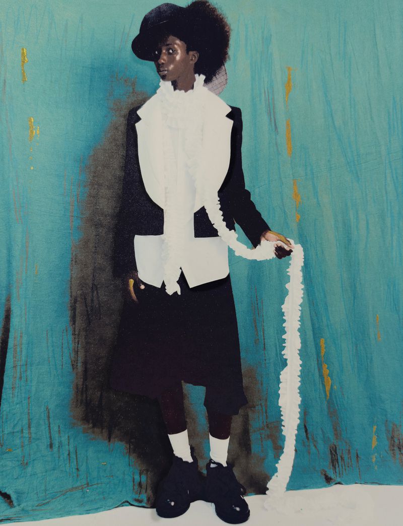 Model Douta Sidibe wearing a black jacket and white ruffled scarf against a textured turquoise backdrop for HERO Magazine