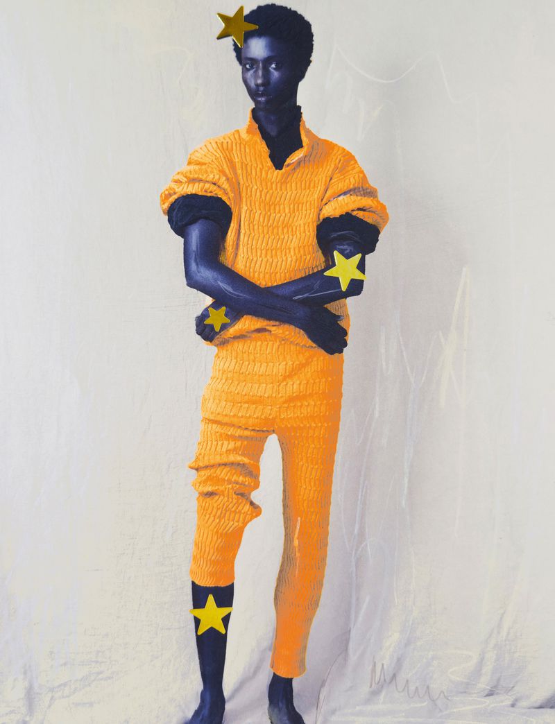 Full-length fashion shot of a model with an altered skin tone wearing a yellow textured outfit with decorative gold star appliques.