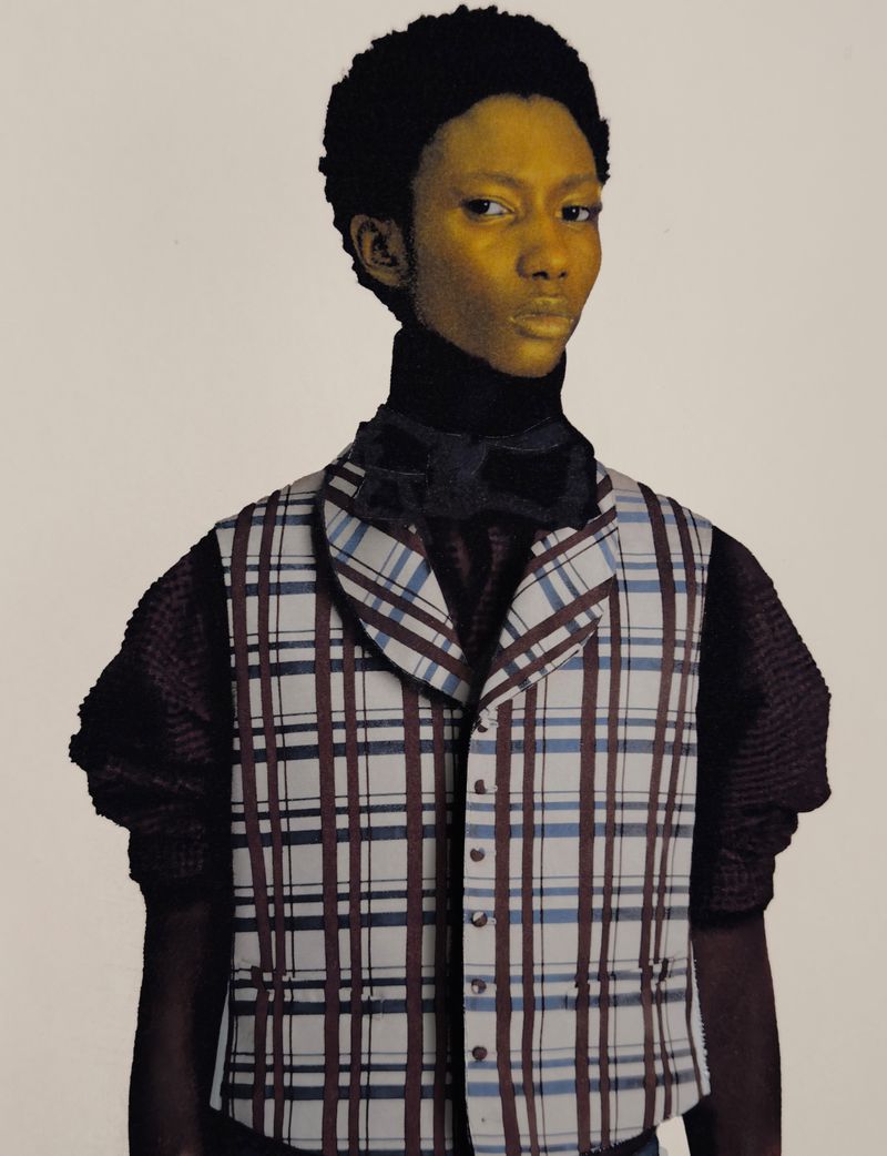 Portrait of androgynous person with dark curly hair, wearing a patterned vest and black turtleneck against a neutral backdrop in studio.