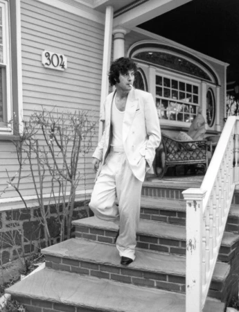 Black and white portrait of a man in a light-colored suit smoking while standing on the steps of a house with the address number 304.