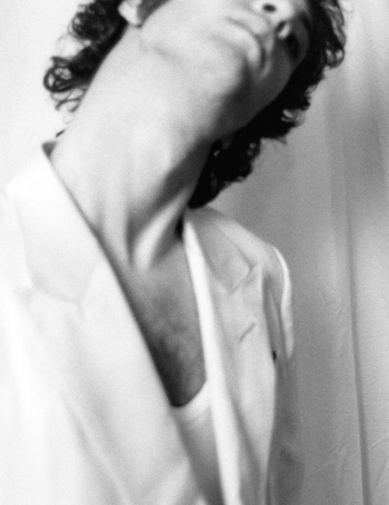 Close-up portrait of Dominic Sessa tilting his head back, wearing a white blazer and tank top against a white backdrop.