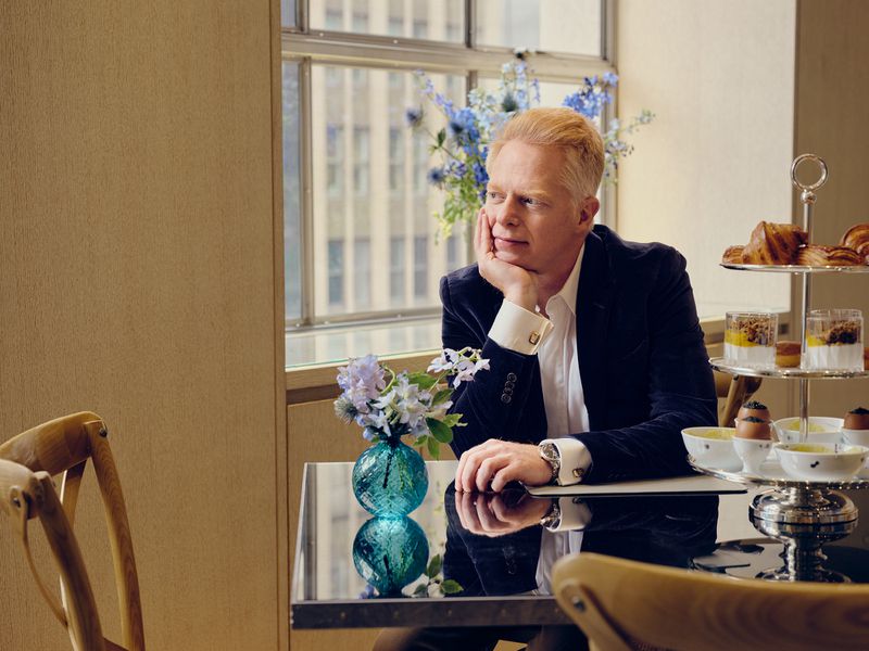 Adult male sitting at a table in front of a window with a building in the background, enjoying an afternoon tea service.