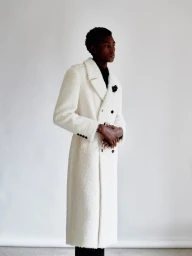 Black man wearing a long white textured coat against a neutral studio background for HERO Magazine