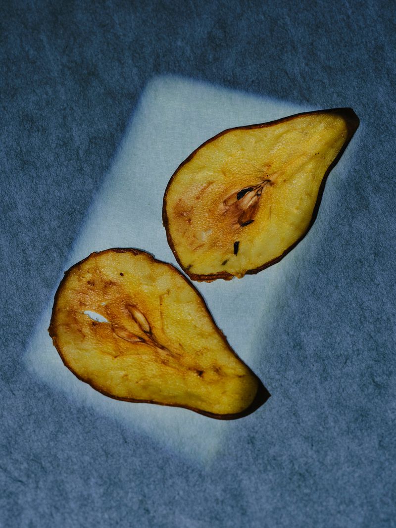 Two pear halves with visible seeds displayed on textured surface in studio lighting, ideal for healthy eating or food photography concepts.