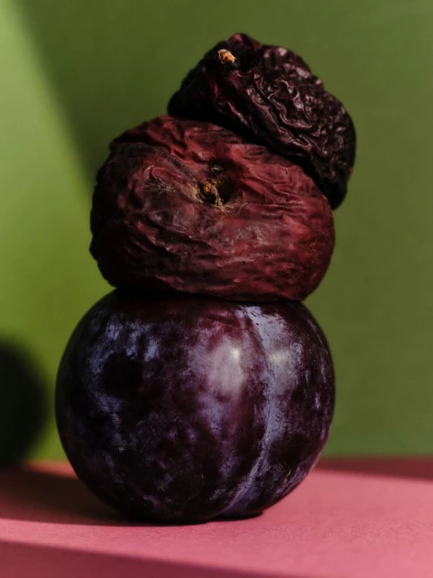Close-up studio shot of a stack of plums with varying degrees of ripeness, set against a vibrant green and pink backdrop.