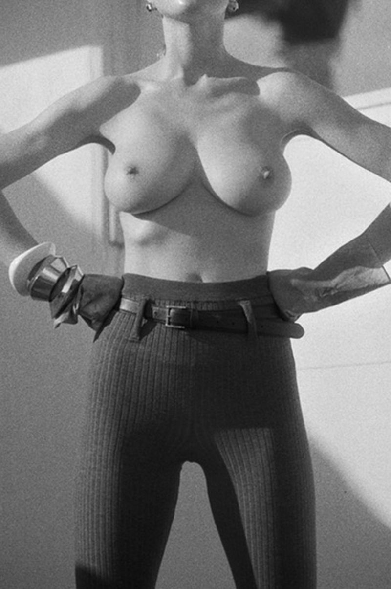 Black and white studio shot of an adult female posing with hands on hips, wearing fitted pants, a belt, and a bracelet. 