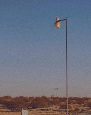 A tall metal street light in a desert setting under a clear sky. The light's design is vintage, casting a warm glow on the arid landscape.