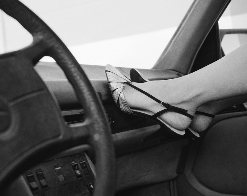 Black and white shot of a woman's feet in black high heels on the dashboard of a vintage car, focusing on style and automotive detail.